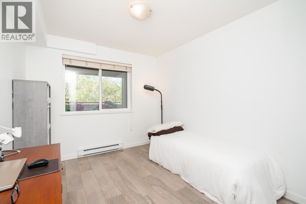 Small bedroom with a single bed, desk, and a window with a garden view. - 303 160 Shoreline Circle, Port Moody