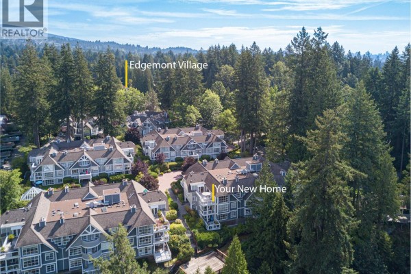 Aerial view of the apartment complex nestled amongst tall trees with a distant city and water view. - 303 3373 Capilano Crescent, North Vancouver