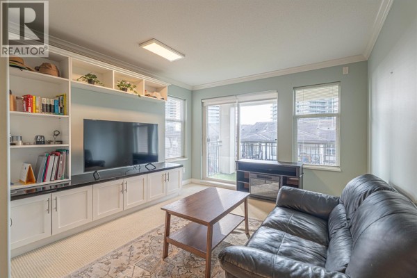 Living room with built-in shelving, large TV, and leather sofa, leading to balcony. - 303 4799 Brentwood Drive, Burnaby