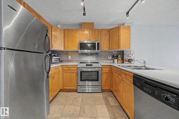 U-shaped kitchen with light wood cabinets, stainless steel appliances, and tiled flooring. - #303 530 Hooke Rd Nw, Edmonton