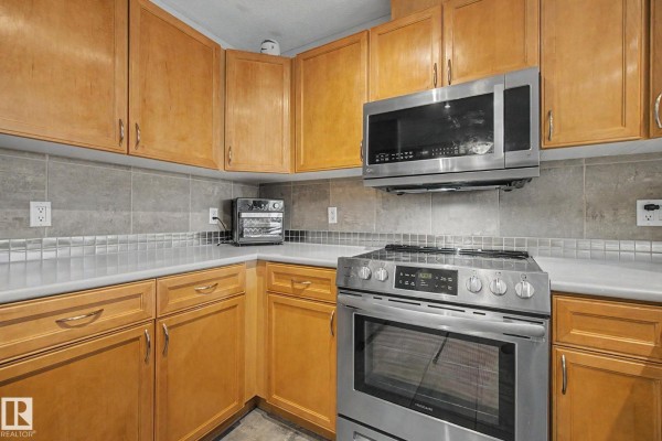 Corner kitchen view showing light wood cabinets, stainless steel stove, and tiled backsplash. - #303 530 Hooke Rd Nw, Edmonton
