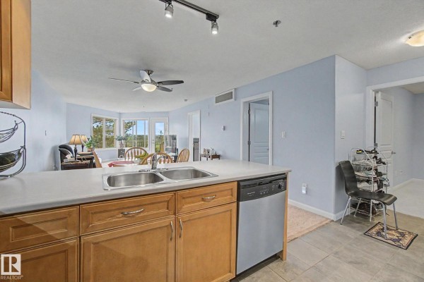 View from kitchen island looking towards living area with dining table and large windows. - #303 530 Hooke Rd Nw, Edmonton