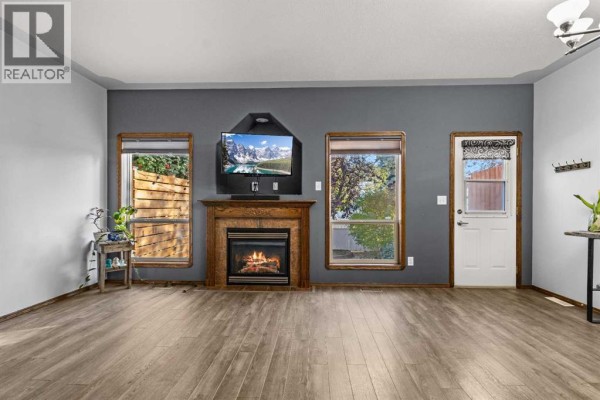 Living room with grey walls, gas fireplace, television, and wood trim windows. - 303 Addington Drive, Red Deer