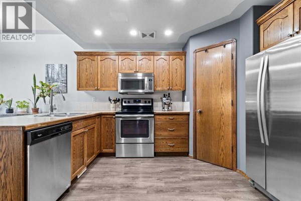 Kitchen with oak cabinets, stainless steel appliances, double sink, and tiled backsplash. - 303 Addington Drive, Red Deer