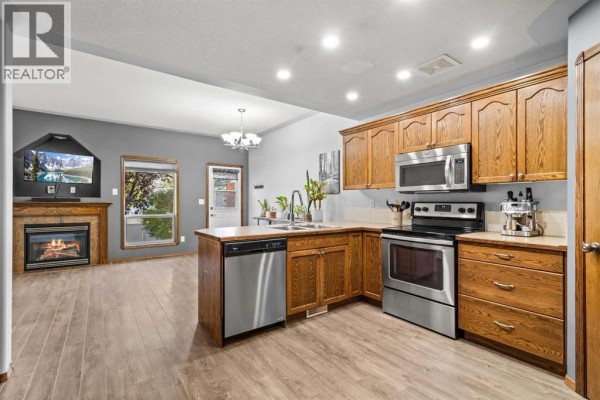 Open concept living and kitchen area with a fireplace, oak cabinets, and island. - 303 Addington Drive, Red Deer