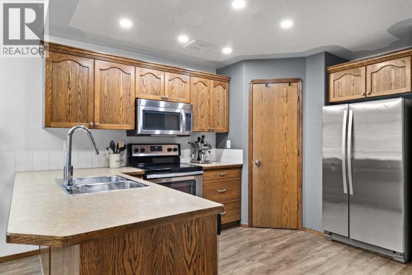 Kitchen view showing oak cabinets, stainless steel appliances, and wood-look flooring. - 303 Addington Drive, Red Deer