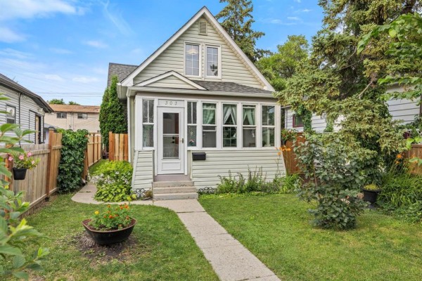 View of the front exterior and sunroom of a light green house. - 303 Chalmers Avenue, Winnipeg