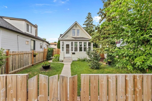 Wooden fence in the foreground with a light green house behind it. - 303 Chalmers Avenue, Winnipeg