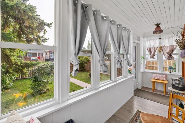 Sunroom interior with multiple windows showing the backyard and light wooden floors. - 303 Chalmers Avenue, Winnipeg