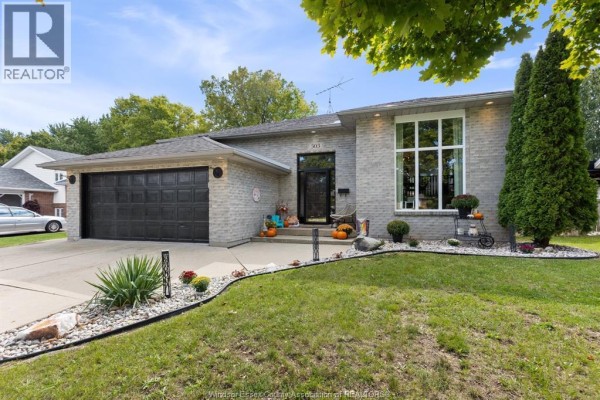 Front exterior of a grey brick bungalow with a black garage door and a large window. - 303 Stone Ridge Avenue, Amherstburg