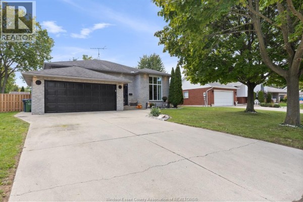 Side view of the grey brick bungalow with a concrete driveway and green lawn. - 303 Stone Ridge Avenue, Amherstburg
