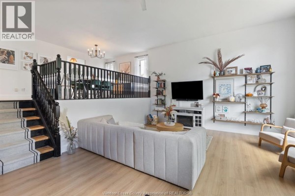 Living room with a sectional sofa, stairs to a raised dining area, and shelves on the wall. - 303 Stone Ridge Avenue, Amherstburg