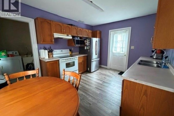 Kitchen with purple walls, wooden cabinets, stainless steel refrigerator, and a round wooden table. - 303 Wellington Street West, Chatham