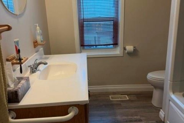 Bathroom with a white vanity, sink, toilet, and a window with blinds. - 303 Wellington Street West, Chatham