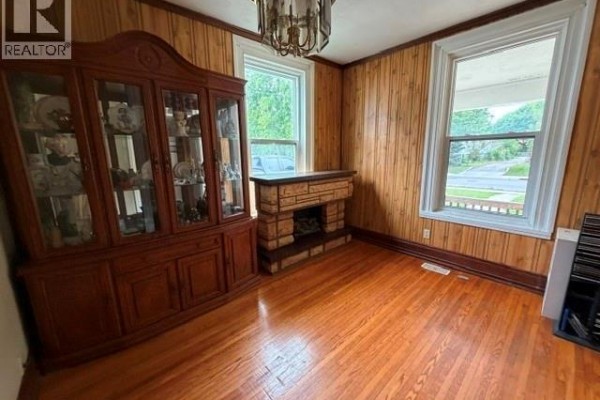 Dining room with wood-paneled walls, hardwood floors, a china cabinet, and a decorative fireplace. - 303 Wellington Street West, Chatham
