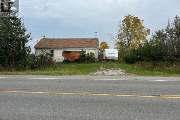 View of the white house from the roadside, showing a driveway with a trailer and large orange equipment. - 3031 Rainham Road, Haldimand