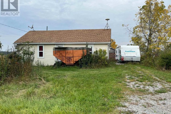 Close-up view of the white house from the side, with an orange trailer and a travel trailer parked nearby. - 3031 Rainham Road, Haldimand