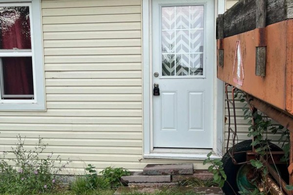 Exterior door of a light-yellow vinyl-sided house with a white paneled door and a small window. - 3031 Rainham Road, Haldimand