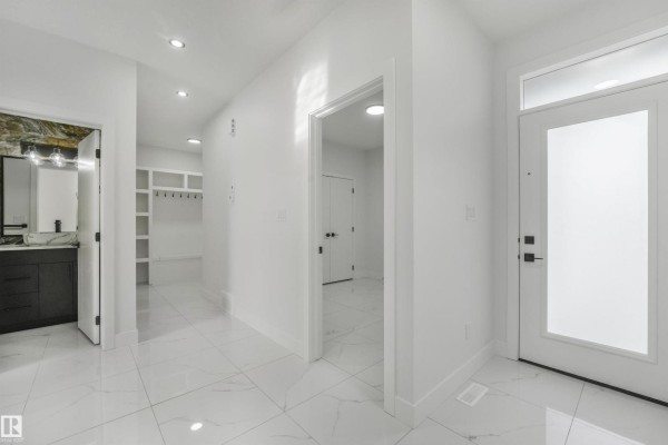 Bright and spacious entryway with white tile floors, white walls, and doorways to other rooms. - 3033 7a Avenue Sw, Edmonton