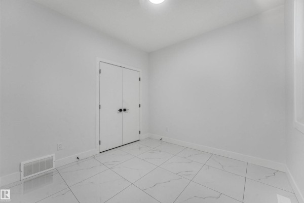 Empty room with white walls, double doors, and large white tile flooring. - 3033 7a Avenue Sw, Edmonton