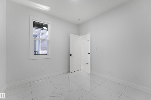 Empty room with white walls, a window showing an exterior view, and white tile flooring. - 3033 7a Avenue Sw, Edmonton