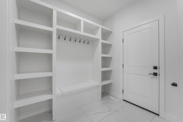 Mudroom with built-in white shelving, coat hooks, a bench, and a closed white door. - 3033 7a Avenue Sw, Edmonton