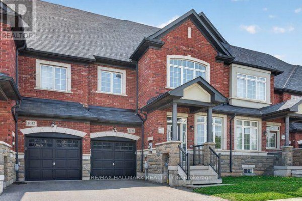 Exterior view of a red brick townhouse with a gray roof and a double garage. - 3034 Eighth Line, Oakville