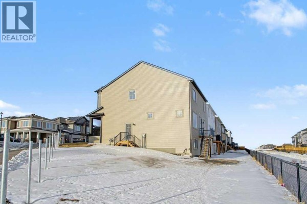 Rear exterior view of the beige house showing a deck and multiple windows. - 3034 Southwinds Place Sw, Airdrie