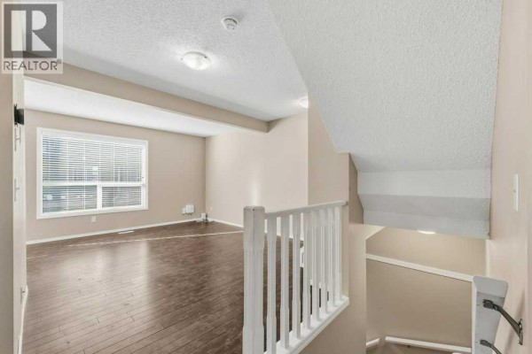 View from the landing overlooking a living area with dark wood floors and a large window. - 304, 140 Sagewood Boulevard Sw, Airdrie