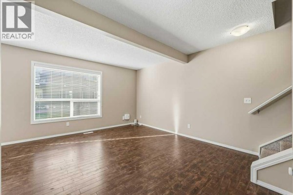 Living room with dark wood floors, beige walls, a large window, and stairs on the right. - 304, 140 Sagewood Boulevard Sw, Airdrie