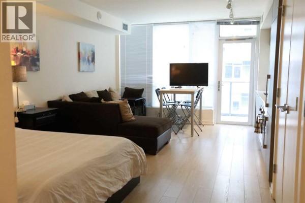 Studio apartment with bed, couch, and dining table, featuring large windows. - 304, 51 Waterfront Mews Sw, Calgary