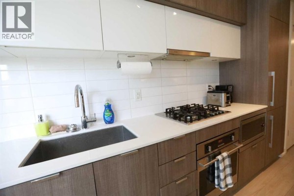 Contemporary kitchen with white cabinetry, gas stove, and stainless steel appliances. - 304, 51 Waterfront Mews Sw, Calgary