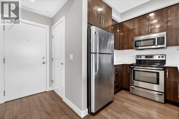Kitchen with dark wood cabinets, stainless steel appliances including a refrigerator, stove, and microwave. - 304, 607 17 Avenue Nw, Calgary