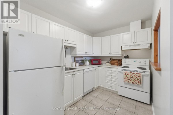 Small white kitchen with white cabinets, white appliances, and light beige tile flooring. - 304 - 110 Forward Avenue, Ottawa