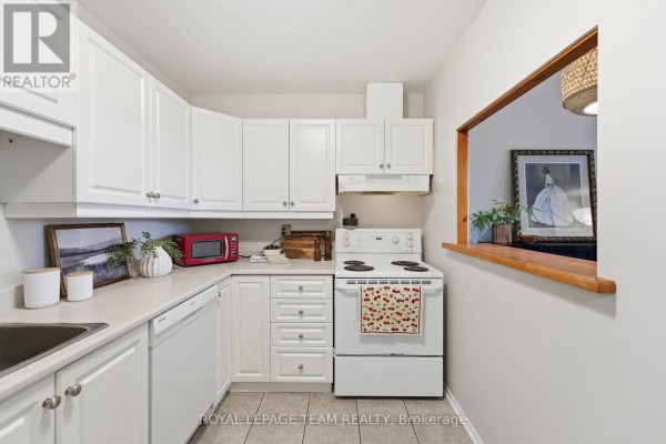 White kitchen with white cabinets, white appliances, and a pass-through window to another room. - 304 - 110 Forward Avenue, Ottawa