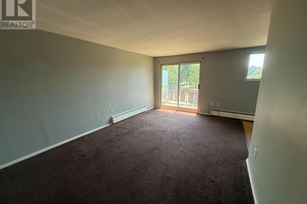 Empty living room with dark brown carpet, grey walls, and a sliding glass door. - 304 - 1830 Dumont Street, London East
