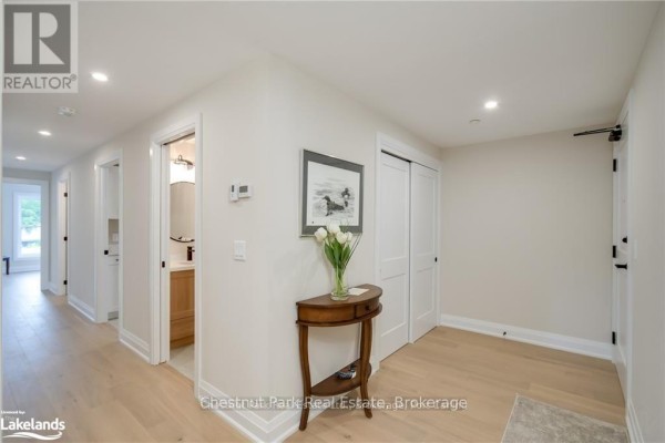 Apartment hallway with light wood floors, white walls, and wooden console table. - 304 - 200 Anglo Street, Bracebridge