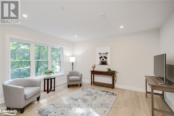 Living room with large bay window, light grey chairs, and modern decor. - 304 - 200 Anglo Street, Bracebridge