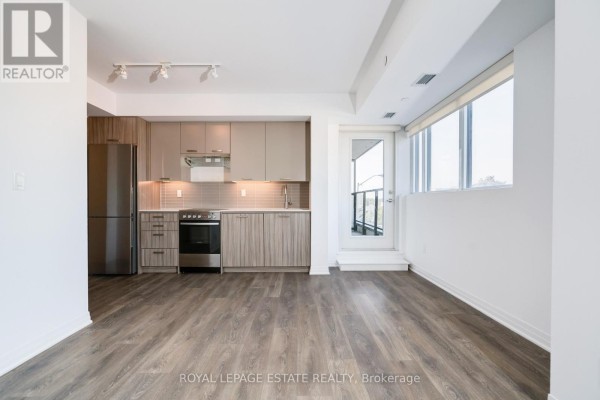 Apartment kitchen with stainless steel refrigerator, light wood cabinets, and view of balcony door. - 304 - 2301 Danforth Avenue, Toronto