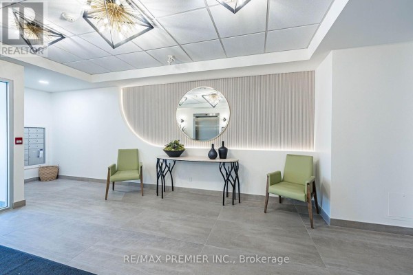Interior building lobby with light grey tile floors, two green chairs, a decorative console table, and a circular mirror. - 304 - 9451 Jane Street, Vaughan