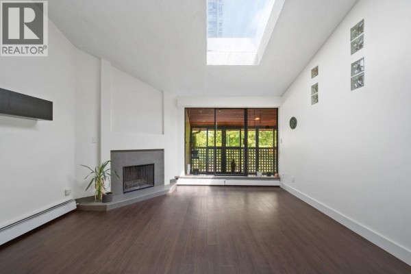 Enclosed balcony with dark wood floors, slatted windows, and potted plants overlooking green trees. - 304 141 W 13th Street, North Vancouver