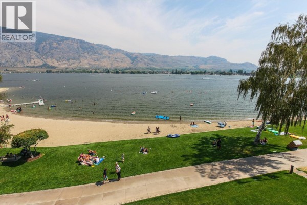 View of sandy beach and lake with people enjoying water activities. - 304-15 Park Place, Osoyoos