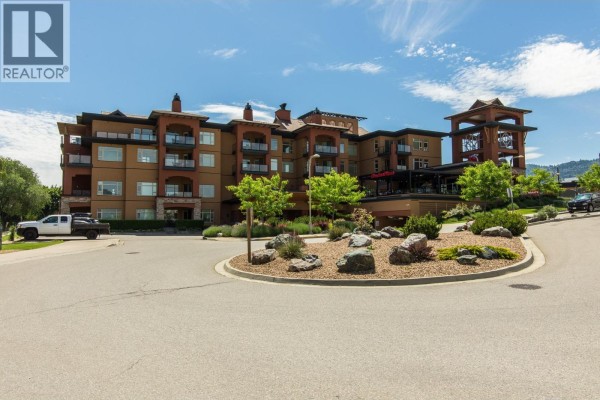 Exterior view of apartment building with landscaped entrance and parking area. - 304-15 Park Place, Osoyoos