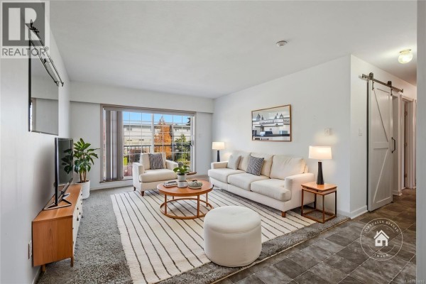 Living room with white sofa, armchair, coffee table, striped rug, and sliding glass door. - 304 266 Hirst Ave, Parksville