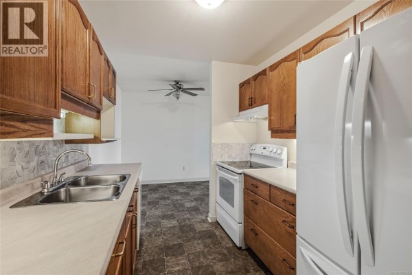 Kitchen with oak cabinets, double sink, white appliances, and patterned backsplash. - 304 266 Hirst Ave, Parksville