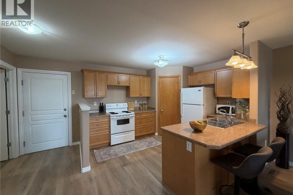 Kitchen with light wood cabinets, white appliances, and granite countertop island. - 304 3730 Eastgate Drive E, Regina