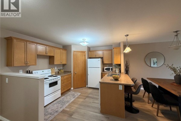 Kitchen and dining area with wood floors, island, and dark wood table. - 304 3730 Eastgate Drive E, Regina