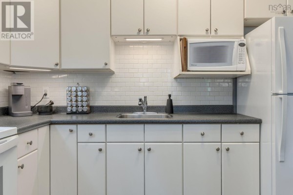 Kitchen area with white cabinets, appliances, and light wood-look flooring inside the apartment. - 304 6369 Coburg Road, South End
