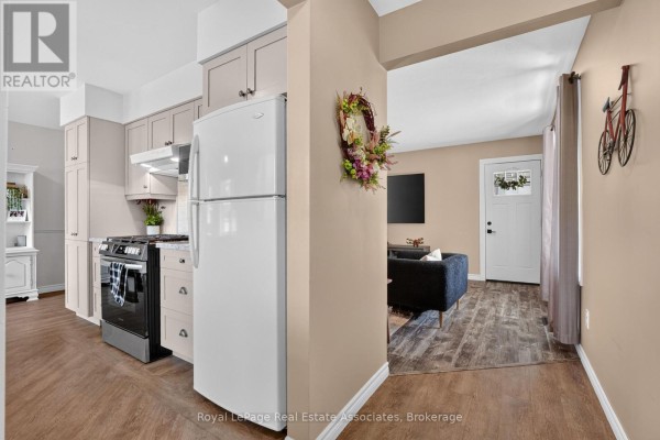 View of the kitchen with a white refrigerator, black stove, and beige cabinets opening into the living room. - 304 Eliza Street, Wellington North
