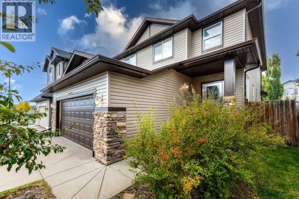 Side exterior view of a house with beige siding, stone accents on the garage pillar, and green bushes. - 304 Evanston View Nw, Calgary